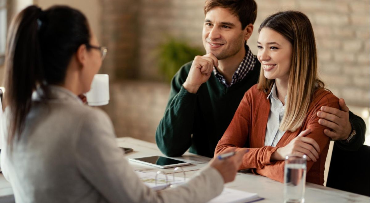 Young Smiling Couple Having Meeting With Financial Advisor Office